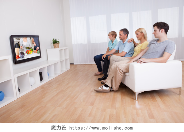坐在白色沙发上一起看电视的家庭家庭看宽屏电视